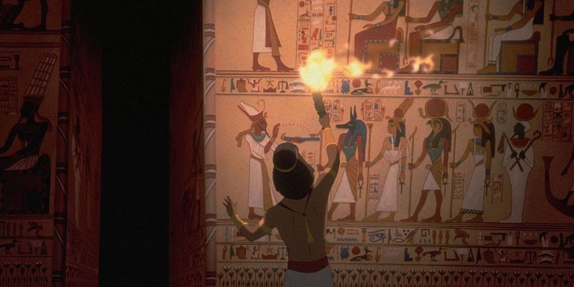 A wide shot of Moses's back, voiced by Val Kilmer, as he holds a flaming torch up to a wall of Egyptian hieroglyphics in The Prince of Egypt