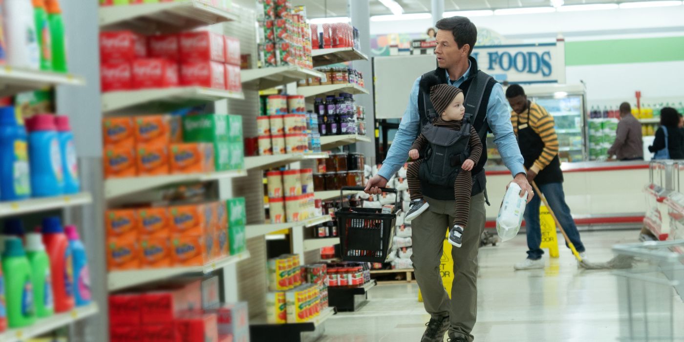 Dan Morgan (Mark Wahlberg) wearing a baby carrier while walking through a grocery store in The Family Plan.
