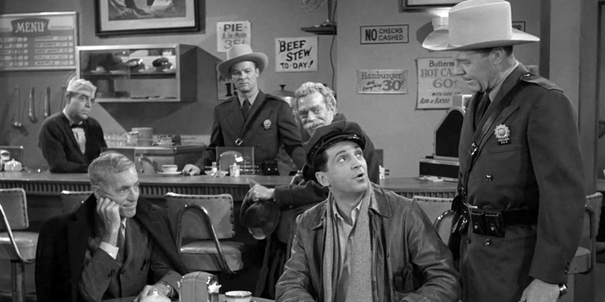 Black and white image of a cop and people in a diner in The Twilight Zone