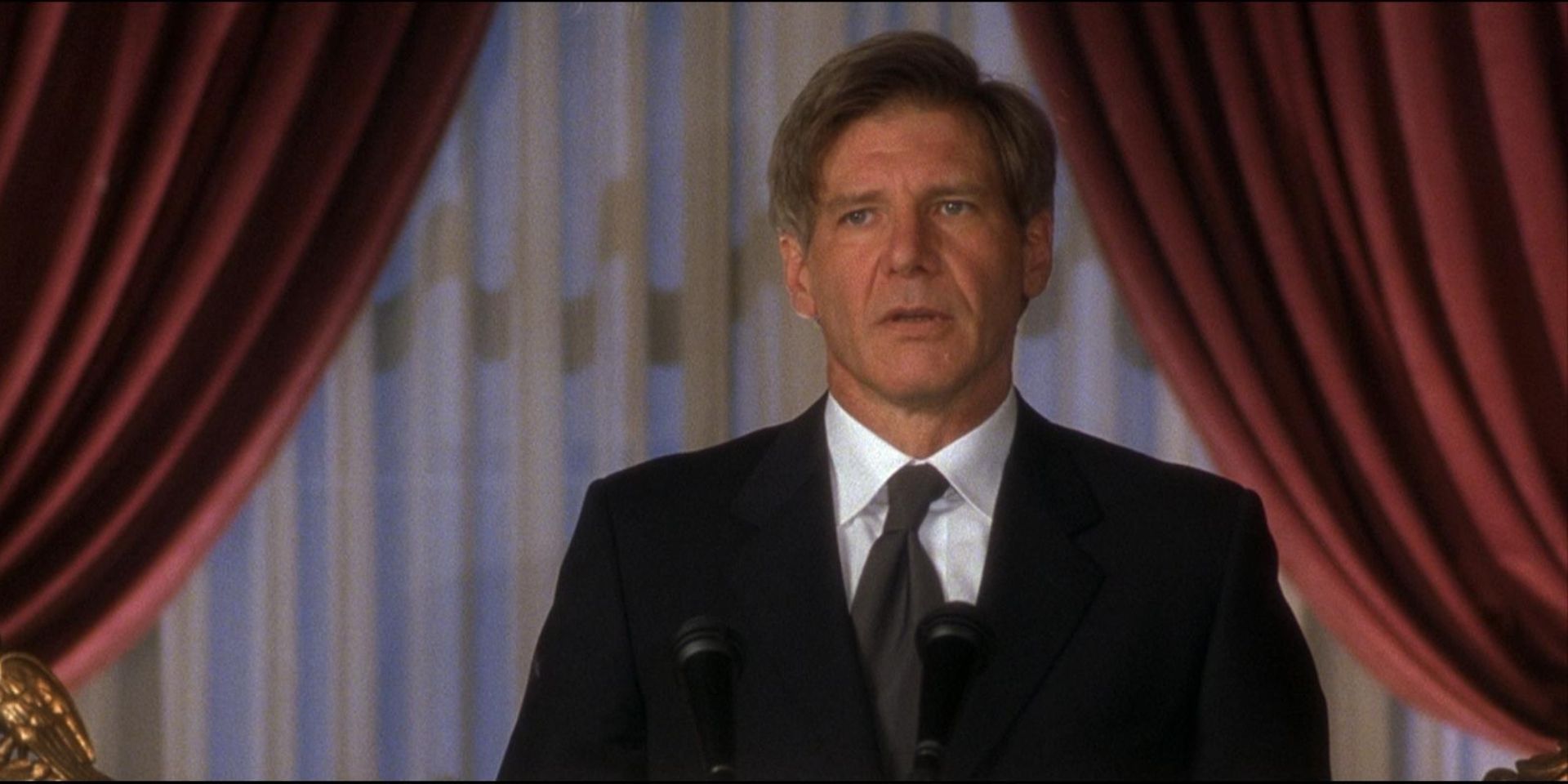 Harrison Ford as President James Marshall standing at a speech podium with a neutral expression in Air Force One