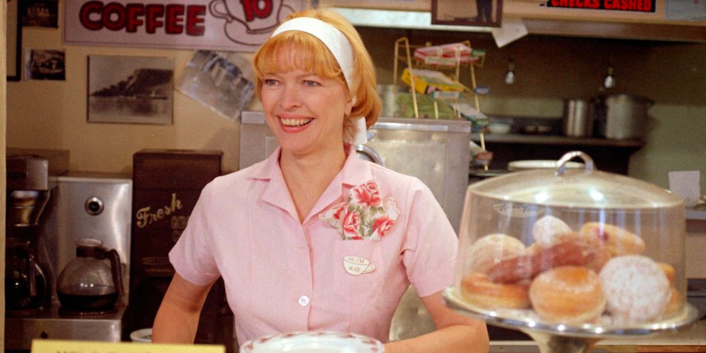 A waitress smiles as she stands behind the counter of a small diner.