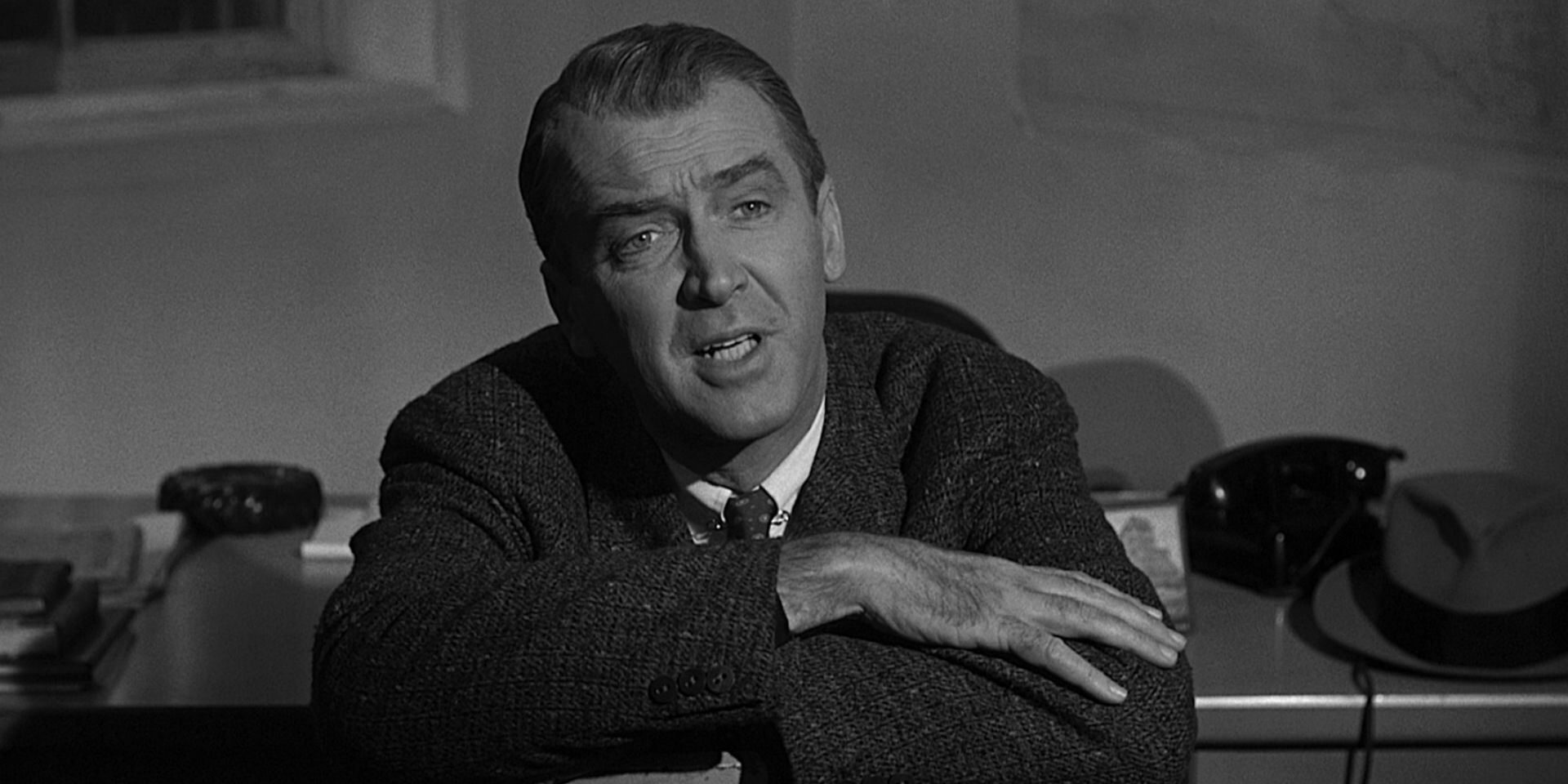Paul Biegler, played by Jimmy Stewart, sitting down and leaning forward with his arms crossed on top of a chair while speaking to someone in Anatomy of a Murder