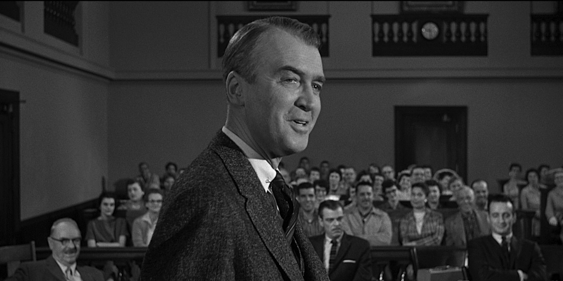 Paul Biegler, played by Jimmy Stewart, standing up and smirking in the courtroom in Anatomy of a Murder