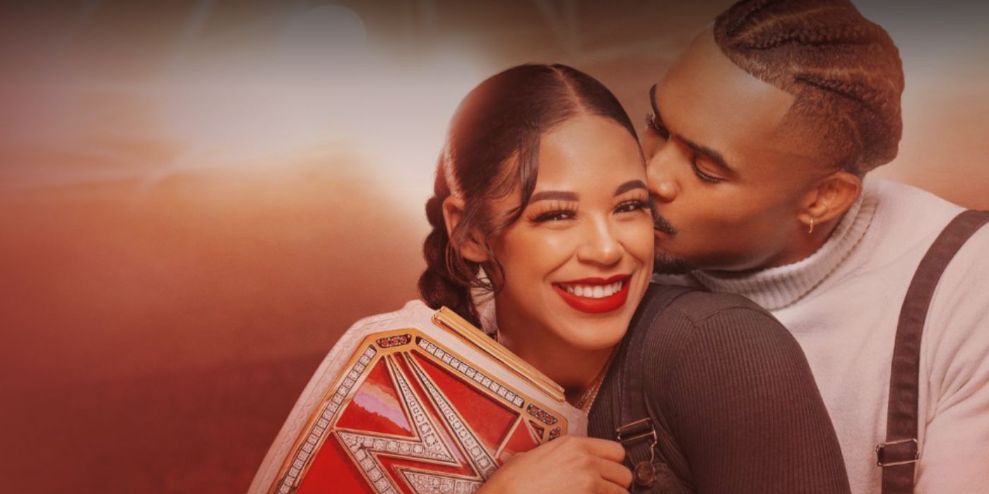 Bianca Belair smiling while Montez Ford kisses her cheek and wraps his arms around her.