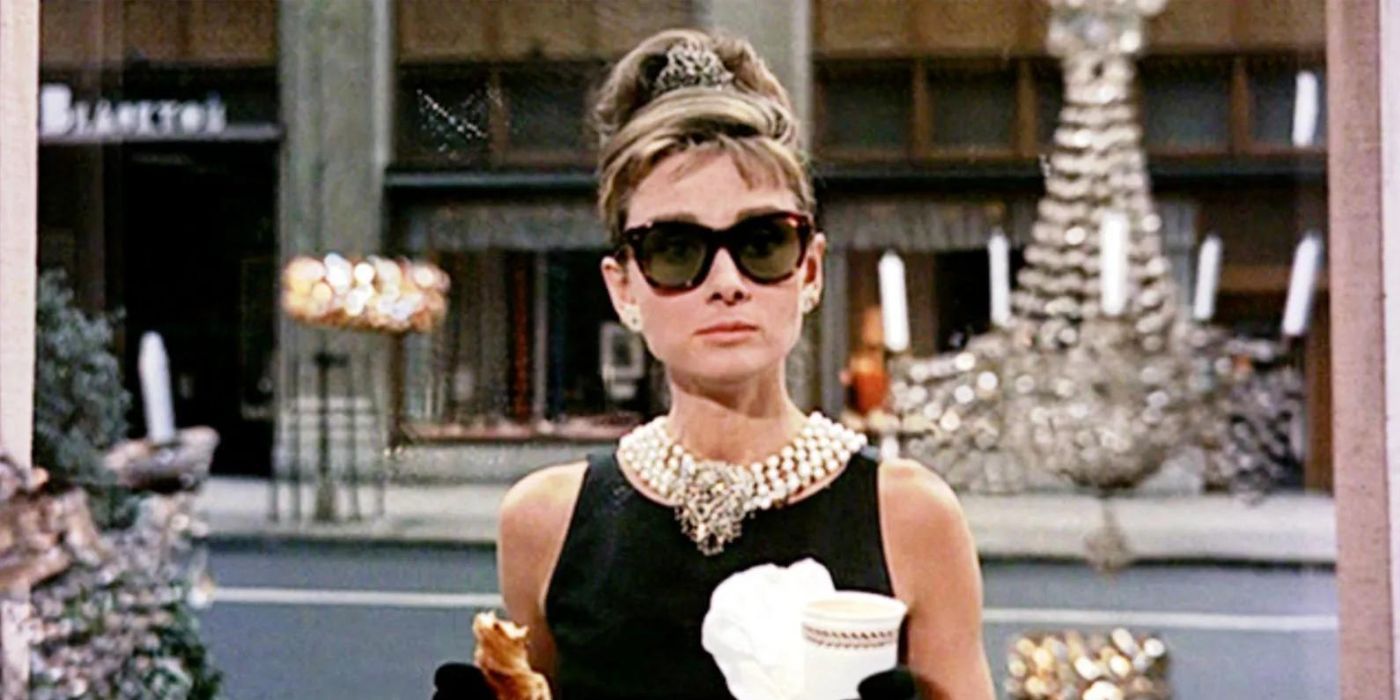 Holly Golightly (Audrey Hepburn) holding a pastry and coffee in front of a shop window in Breakfast at Tiffanys