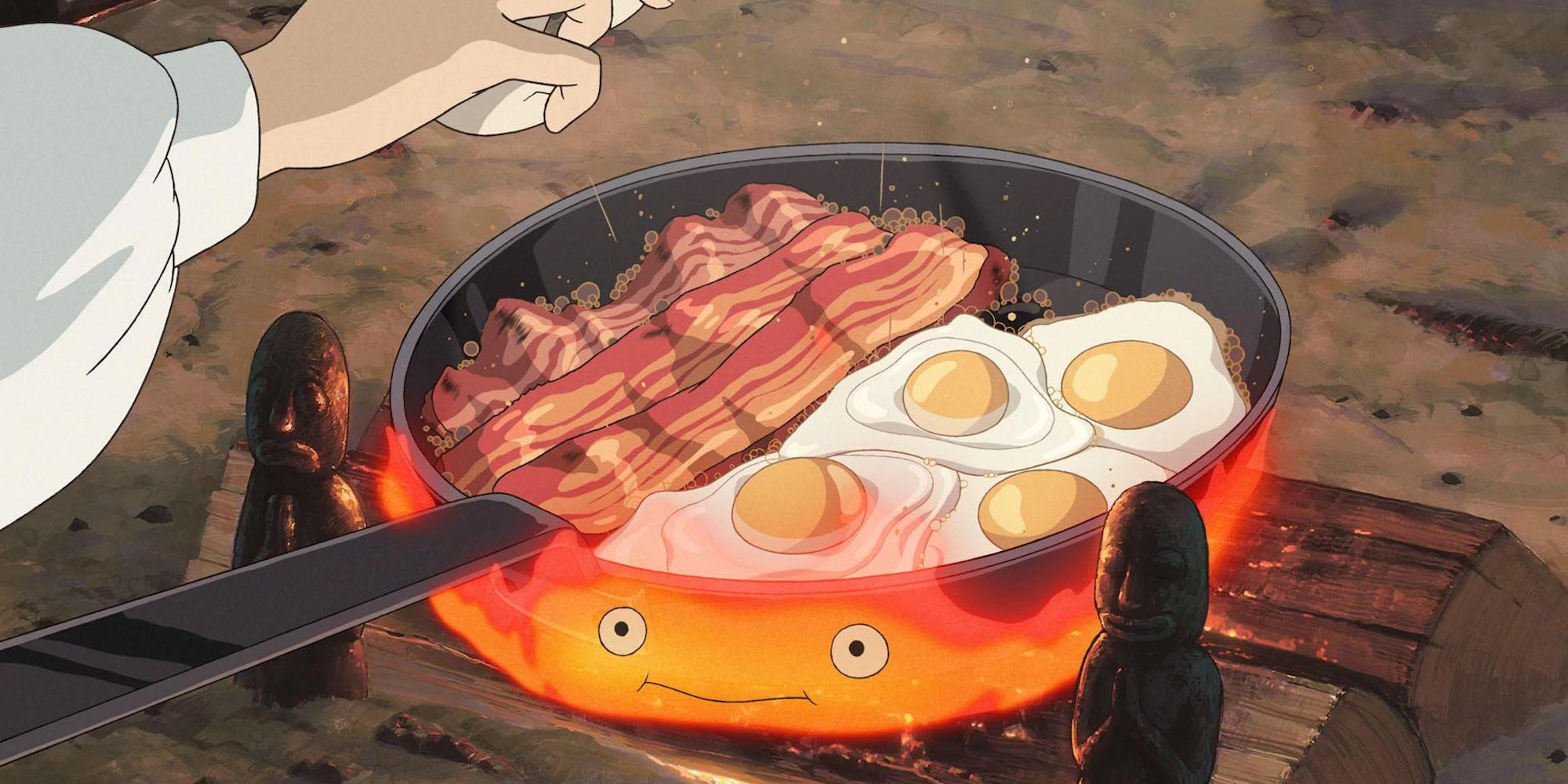 A hand cooking eggs and bacon on a pan in Howl's Moving Castle