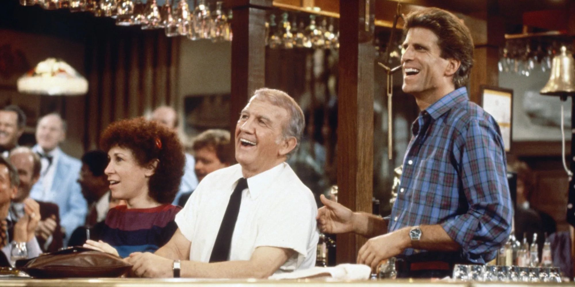 Sam (Ted Danson), Carla (Rhea Perlman), and Coach (Nicholas Colasanto) standing by the bar and laughing in Cheers