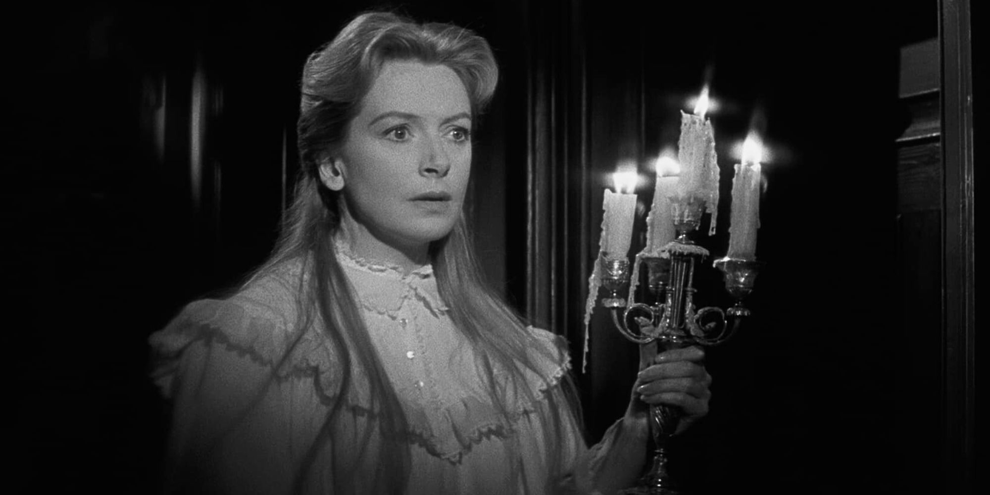 Deborah Kerr standing in a dark hallway holding a candelabra in The Innocents (1961)