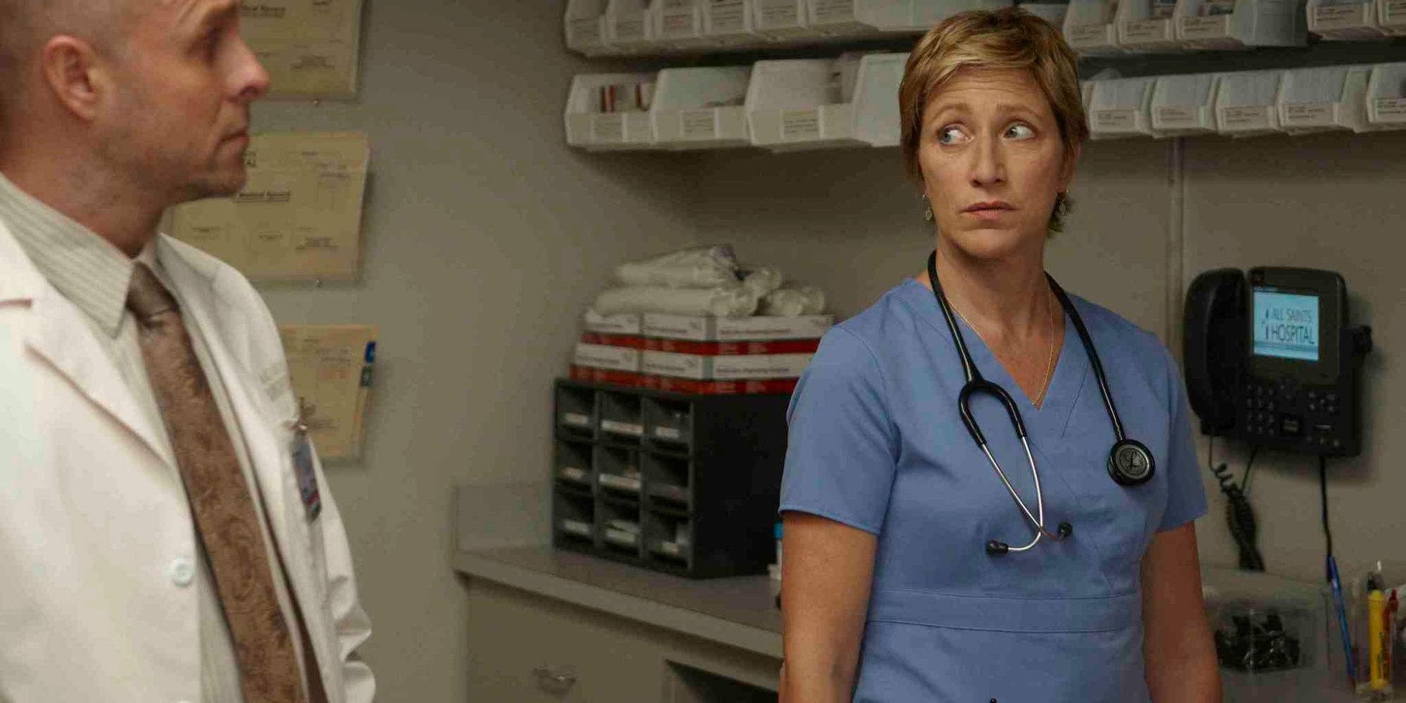 Edie Falco as Jackie and Paul Schulze as Eddie stand in the back office of the pharmacy in Nurse Jackie