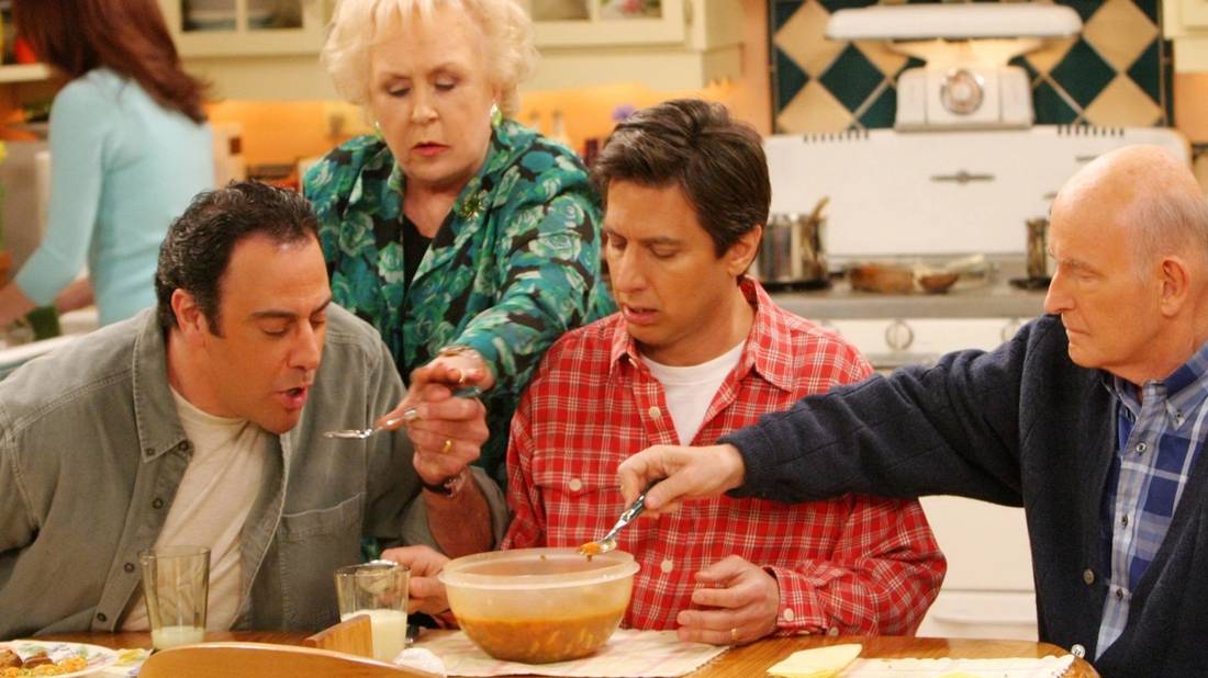 Ray, Robert, and Frank sit at the kitchen table eating as Doris fawns over them in Everybody Loves Raymond.