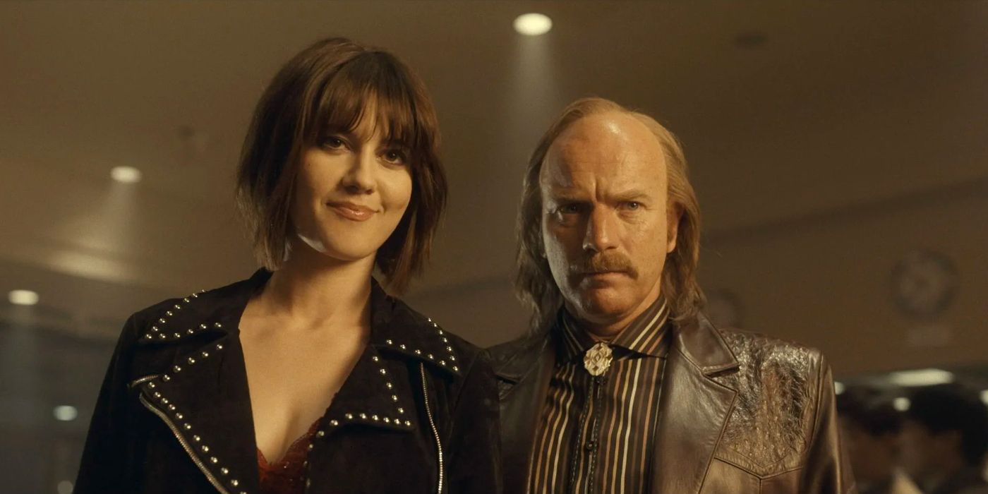 A man in a brown leather jacket stands beside a woman sporting a wicked grin.