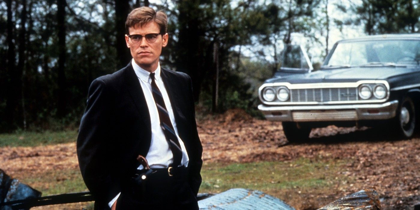 FBI Agent Alan Ward (Willem Dafoe) wears a gun and stands next to a vintage car in Mississippi Burning.