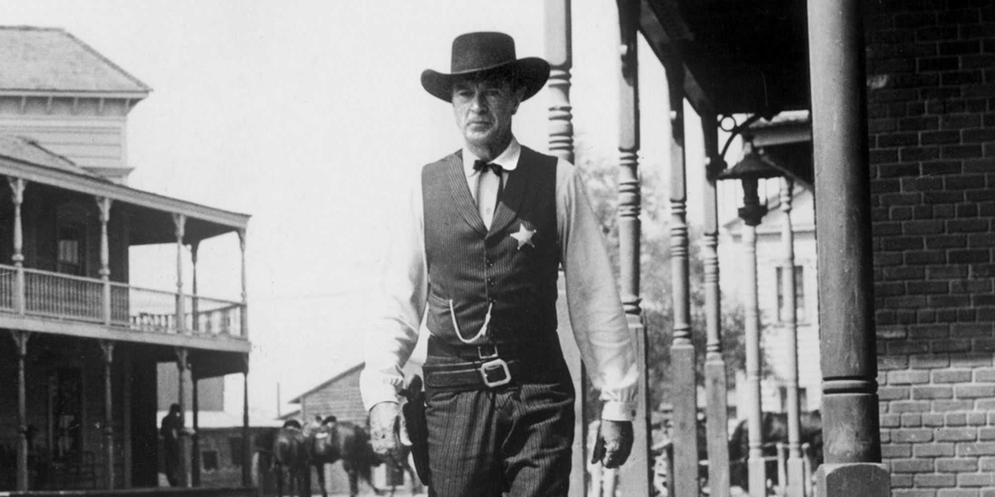 Black and white shot of Gary Cooper walking in a Western village in High Noon.