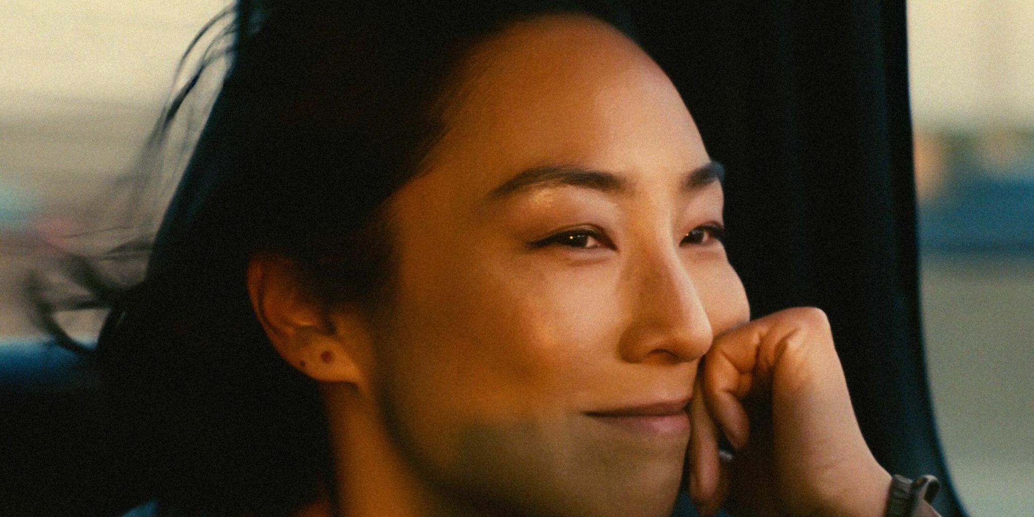 Nora (Greta Lee) smiles while riding in a car in Celine Song's 'Past Lives'