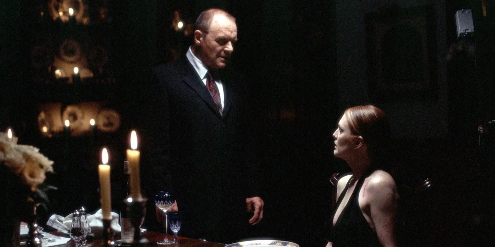 A standing Hannibal Lecter, played by Anthony Hopkins, wearing a black suit and tie and staring down at a sitting Clarice Starling, played by Julianne Moore, wearing a sleeveless black dress in the Hannibal movie