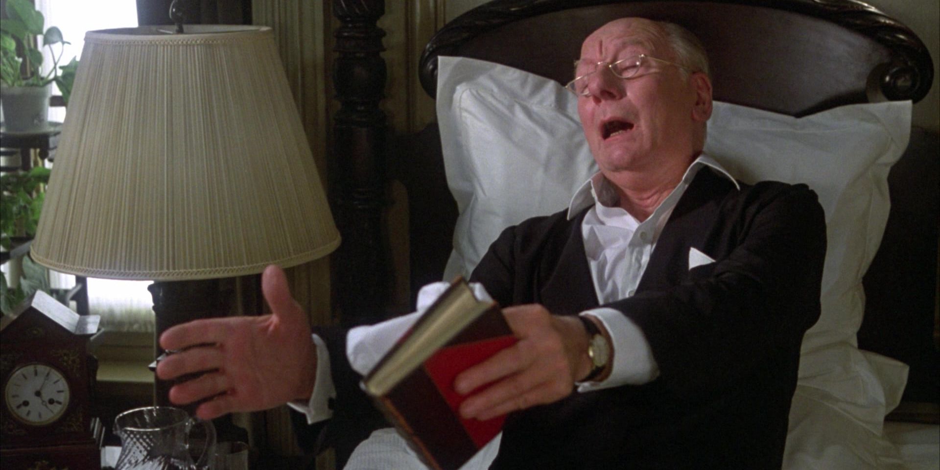 John Gielgud as an old man with glasses sitting on his bed, holding a book in Arthur