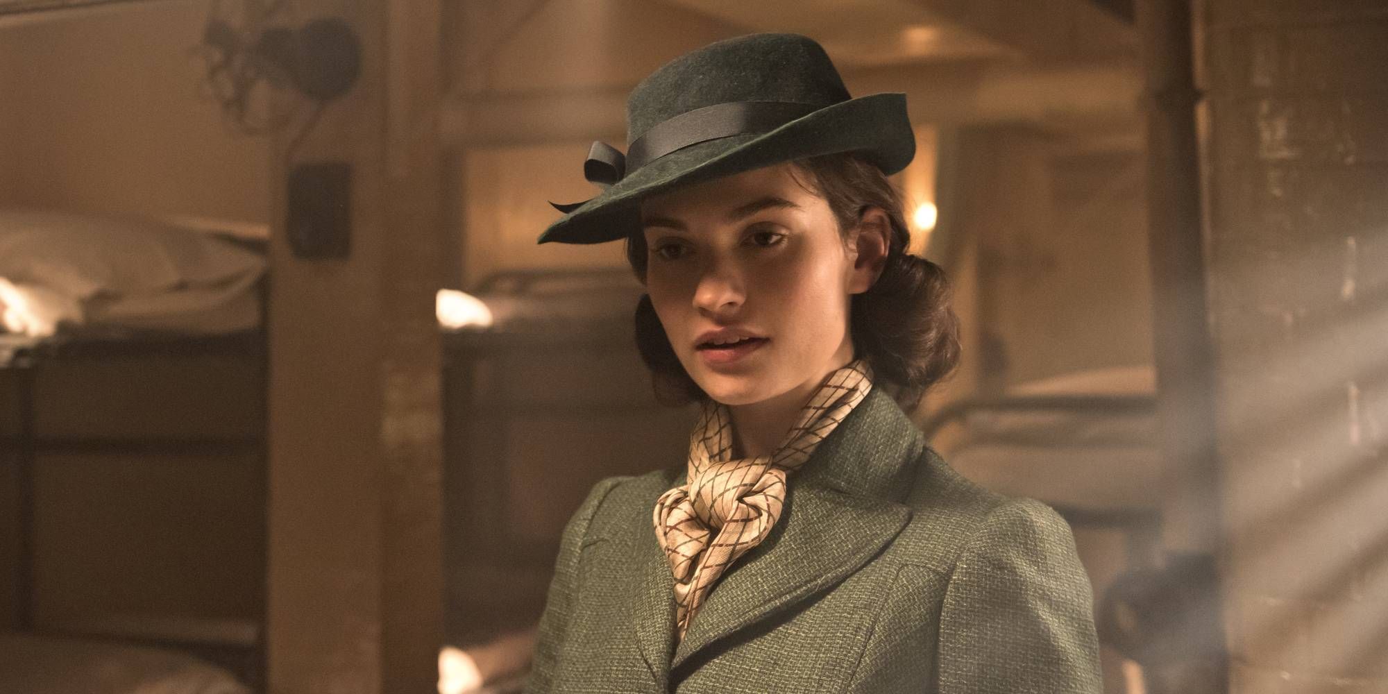 Lily James as Elizabeth Layton, wearing a hat and standing in a dimly lit room in Darkest Hour