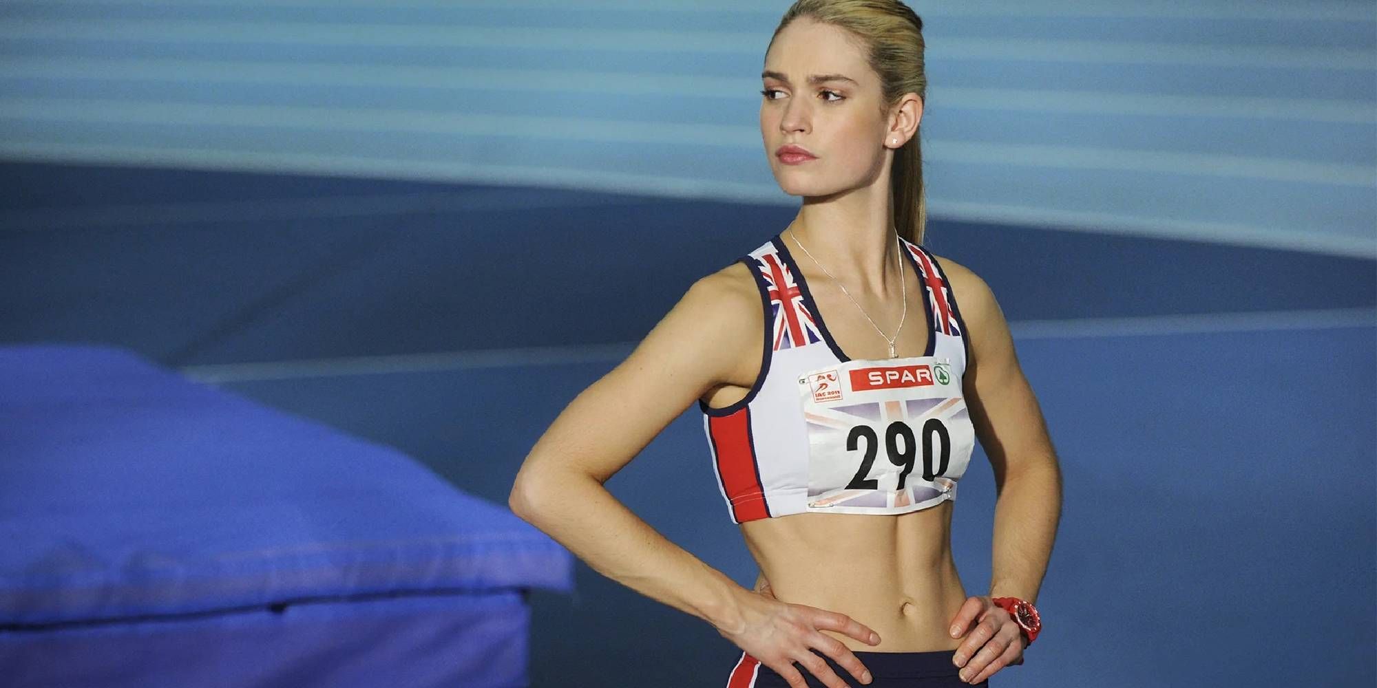Lily James as Lisa Temple, standing in her running uniform with her hands on her hips in Fast Girls