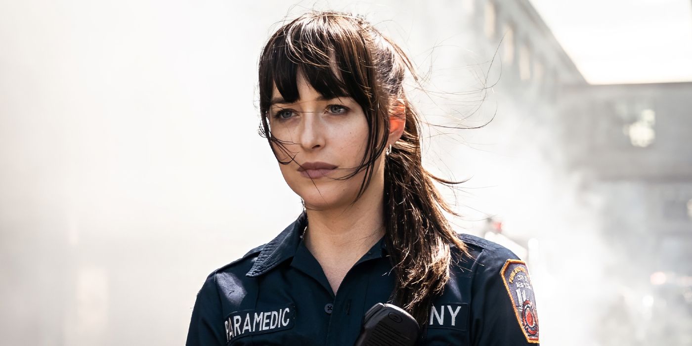 Dakota Johnson wearing a paramedic uniform with firefighters blurred in the background in Madame Web