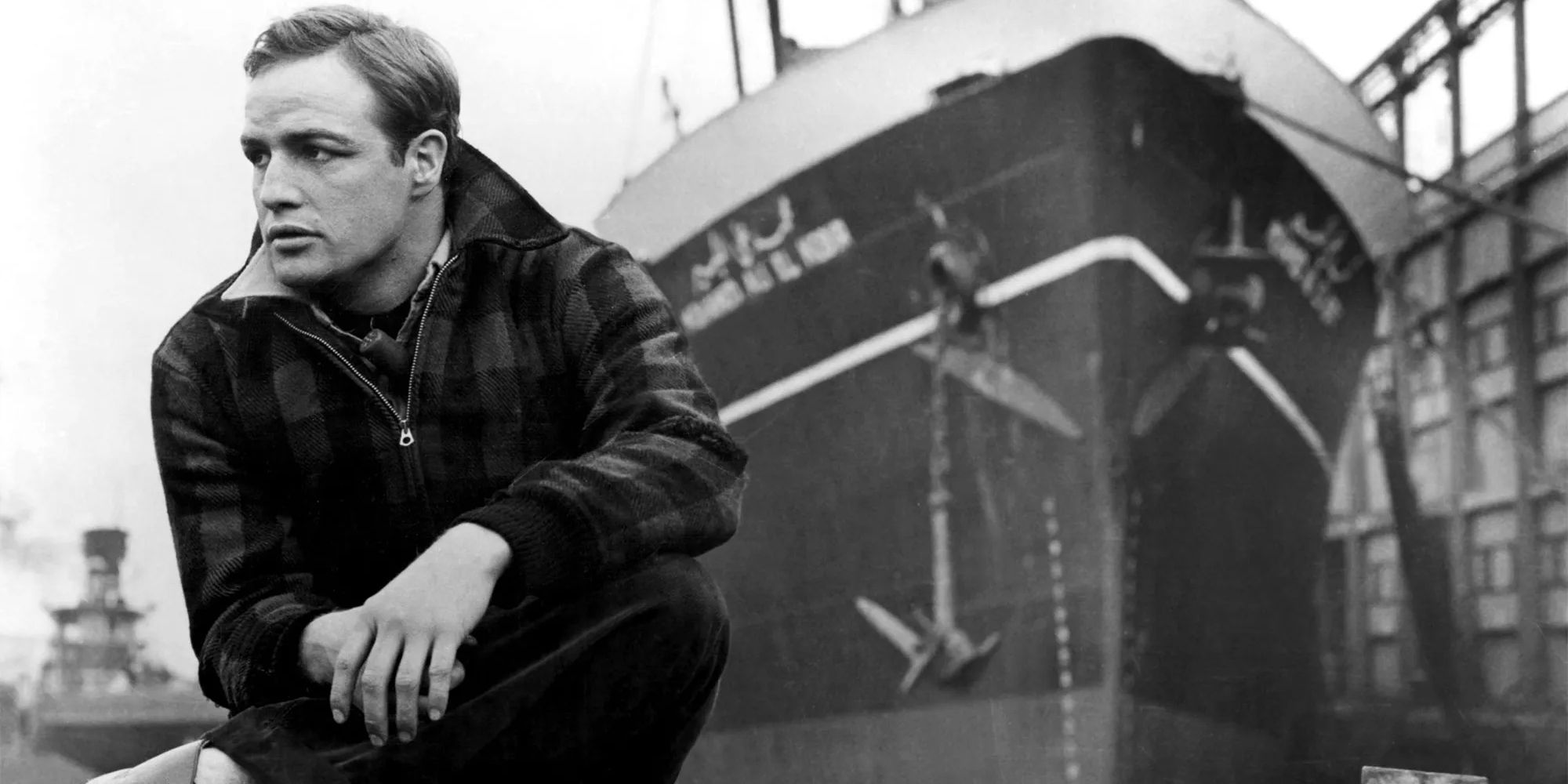 A black and white shot of Marlon Brando sat down in On the Waterfront.