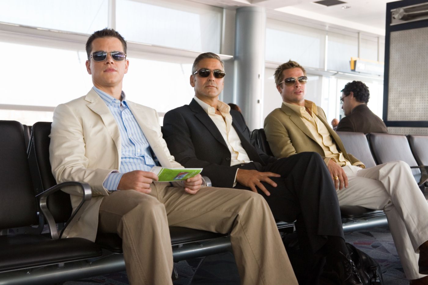 Matt Damon como Linus Caldwell, George Clooney como Danny Ocean e Brad Pitt como Rusty Ryan sentado no saguão de um aeroporto em Oceans Thirteen (1)