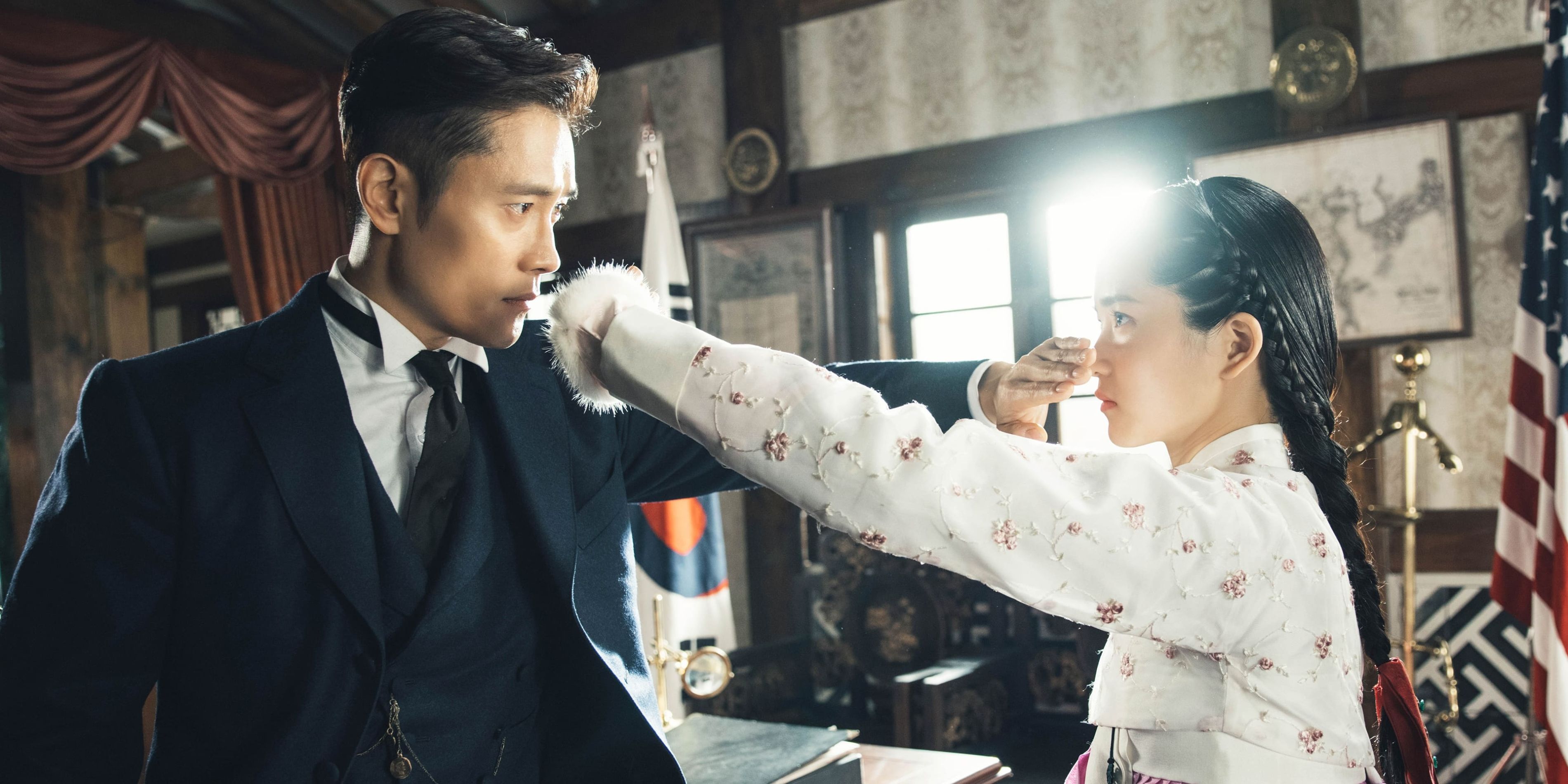 Eugene and Ae-shin, played by Lee Byung-hun and Kim Tae-ri, staring at each other and holding their hands over the lower halves of one another's faces in Mr. Sunshine