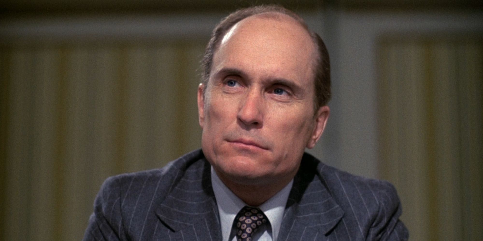 Robert Duvall as Frank Hackett, wearing a suit and looking seriously at something offscreen in Network