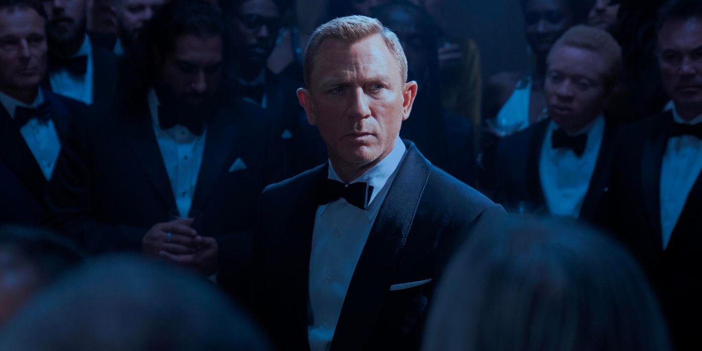 James Bond stands in a tuxedo in a busy party, looking around suspiciously as a spotlight picks him out.