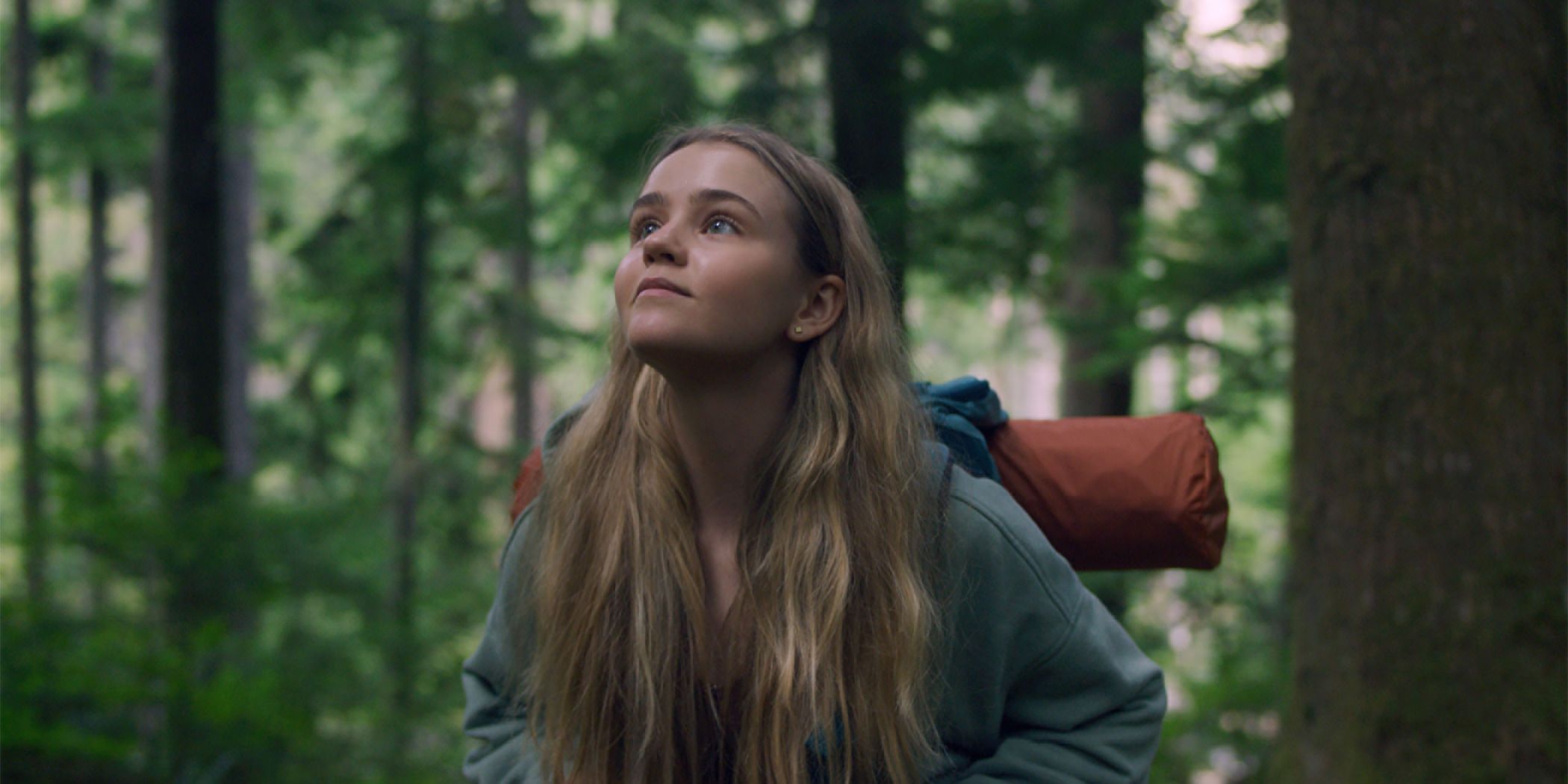 Megan Stott looking up into the trees in a forest in Penelope for Sundance 2024