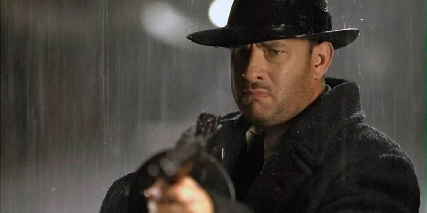 Tom Hanks scowls as he holds up a tommy gun in the pouring rain. 