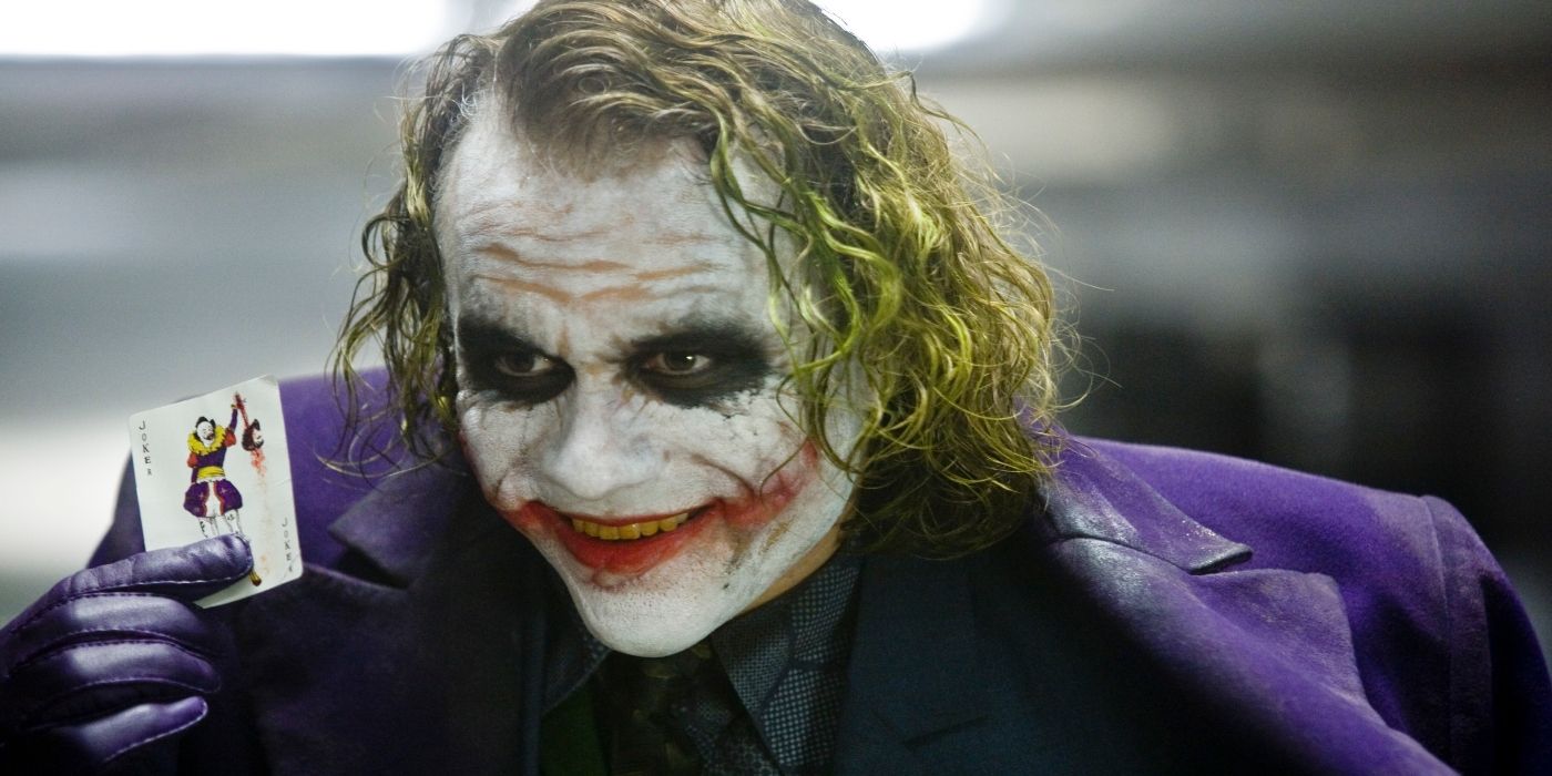 Heath Ledger as The Joker smiling while showing off a joker card in The Dark Knight
