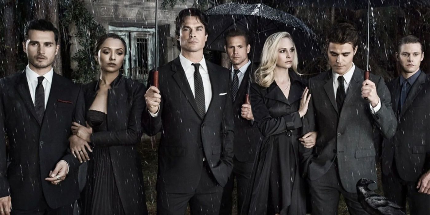 Ian Somerhalder, Paul Wesley, Candice King, and the cast of 'The Vampire Diaries' wearing black and holding umbrellas in the rain.