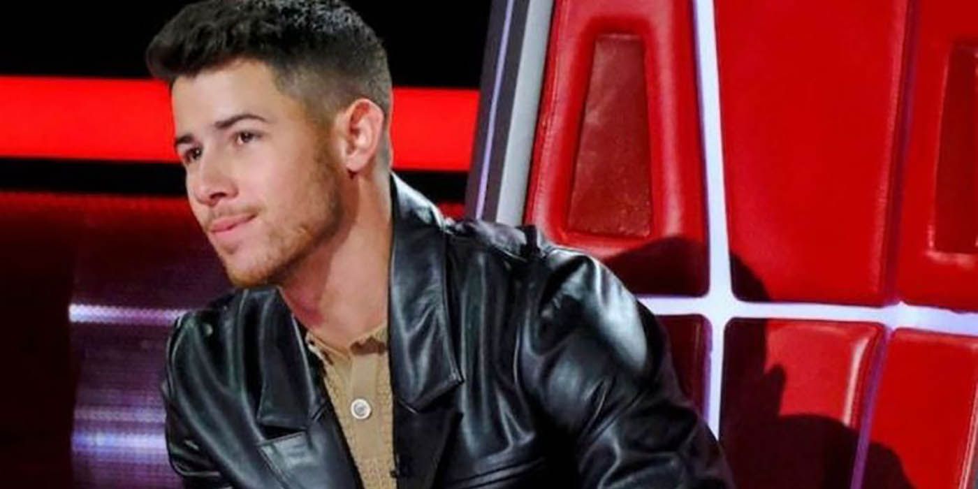 A close up of Nick Jonas on The Voice leaning forward in his chair and listening