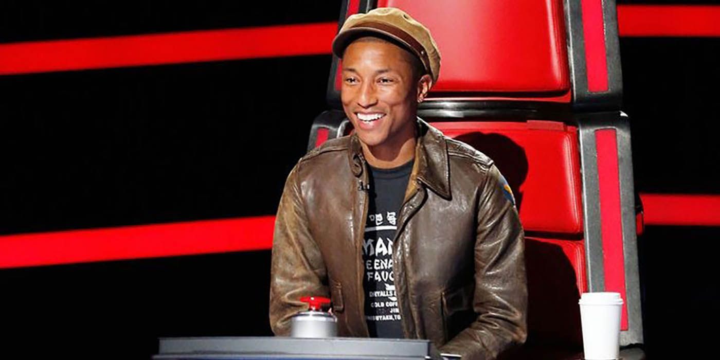 Pharrell sitting in his chair on 'The Voice' smiling widely.