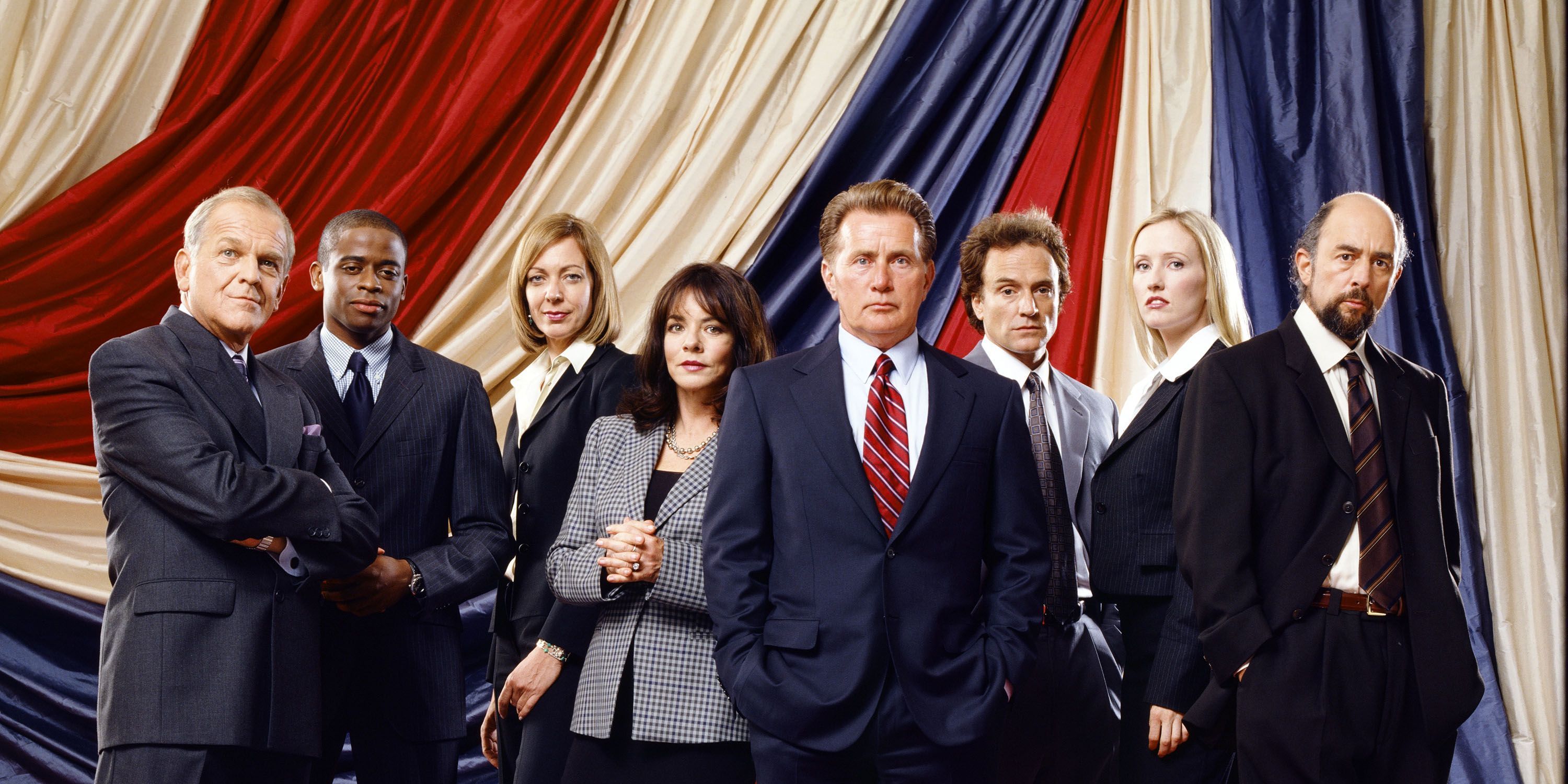 The West Wing cast in front of a red, white and blue curtain