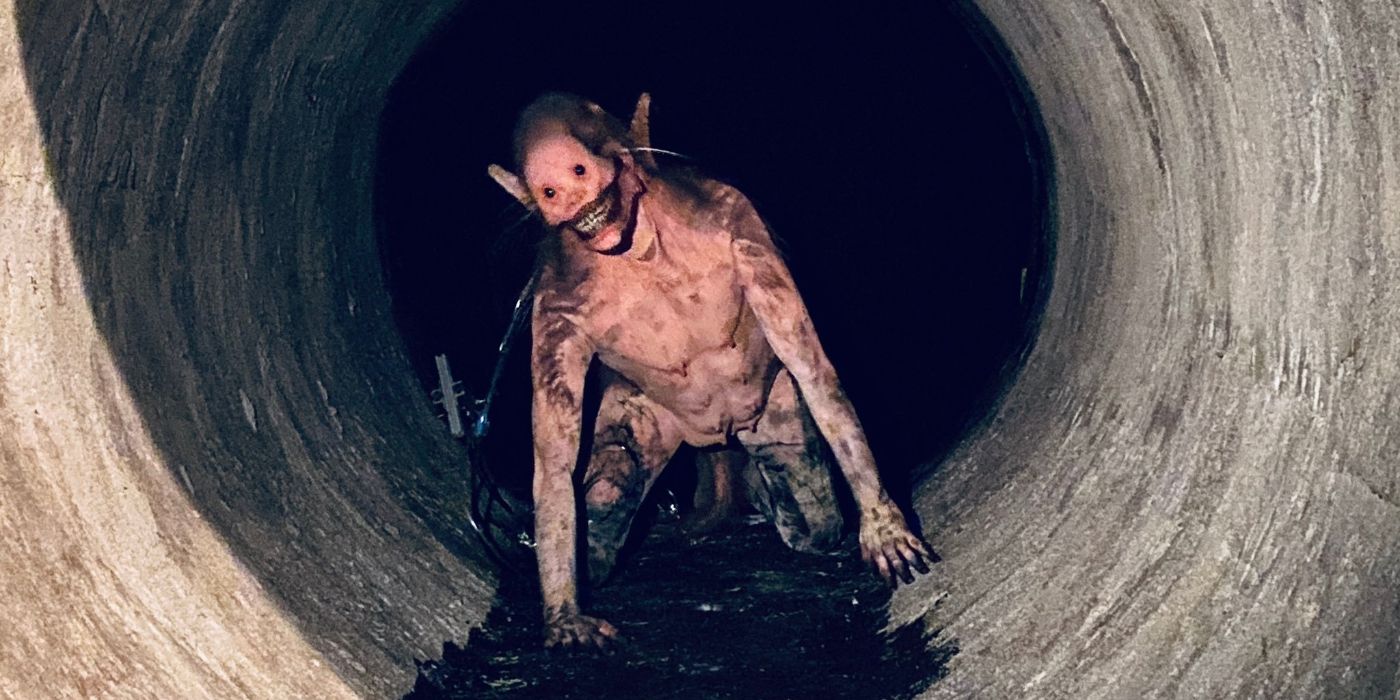 A disturbing half-man, half-rat creature crawls from a storm water drain with a wretched grin on its face.