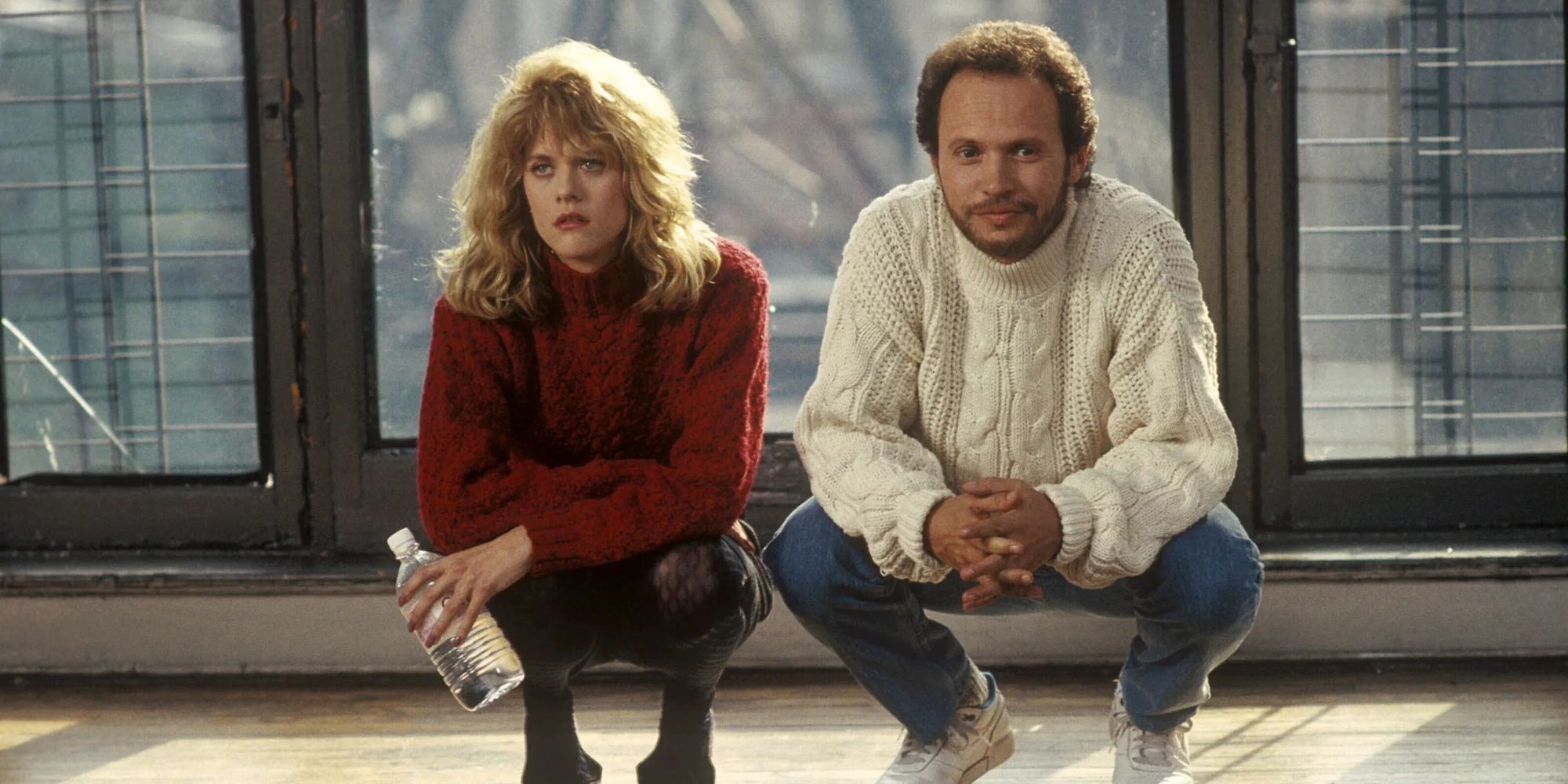 Meg Ryan in a red sweater and Billy Crystal in a white sweater crouching down in When Harry Met Sally