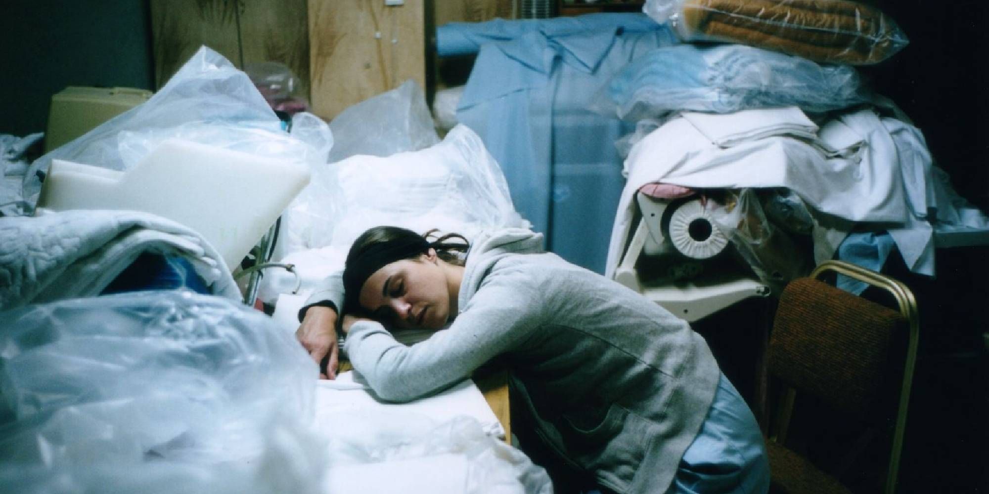 A woman sleeping over a pile of clothes on a desk in Kinetta.