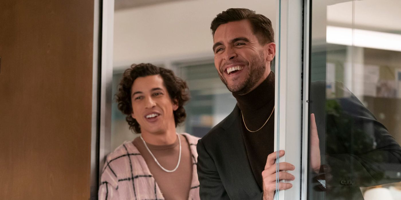 Josh Segarra as Manny laughs in an office doorway with another costar in Abbott Elementary.