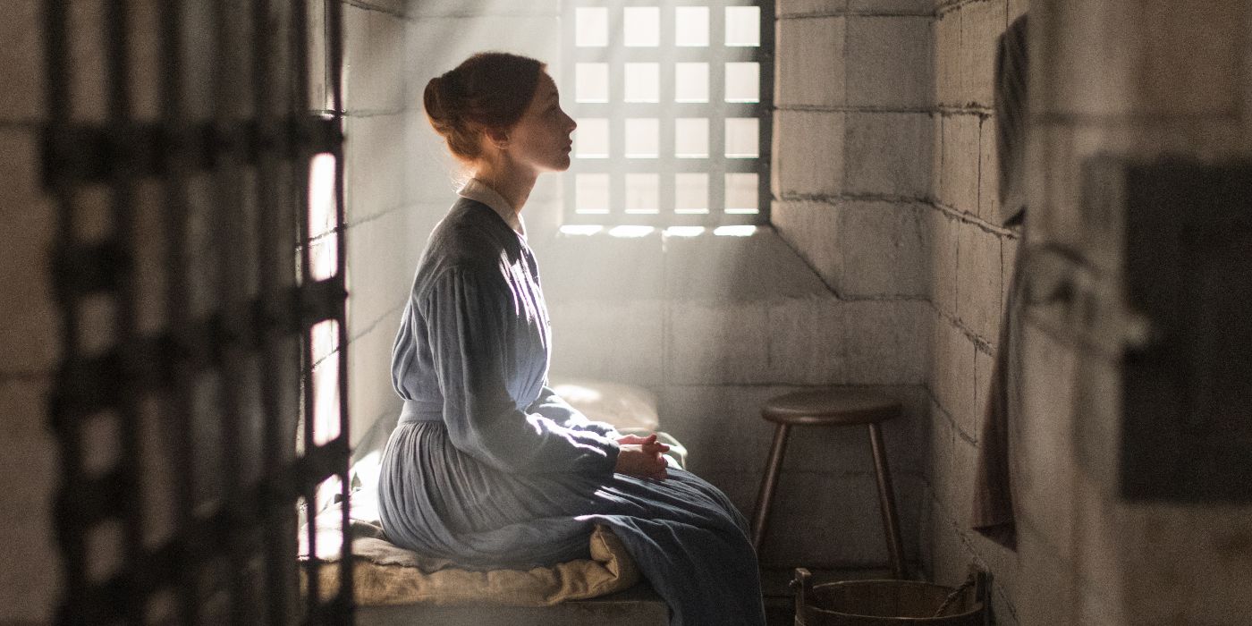 Sarah Gadon, interpretando a Grace Marks en Alias ​​​​Grace, está sentada en un catre en una celda de la prisión, de cara al muro de piedra a su derecha, absorbiendo la luz del sol que entra por la ventana.