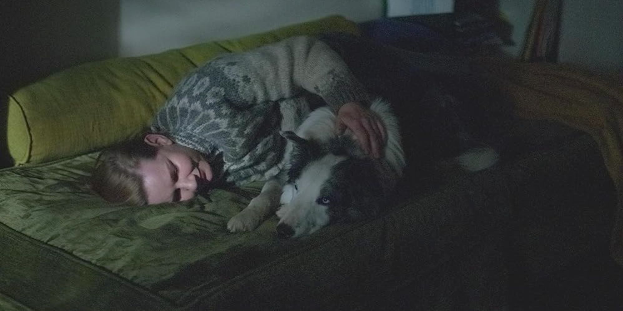 Sandra Hüller as Sandra Voyter, lying on a sofa in a dark room and hugging her dog in Anatomy of a Fall