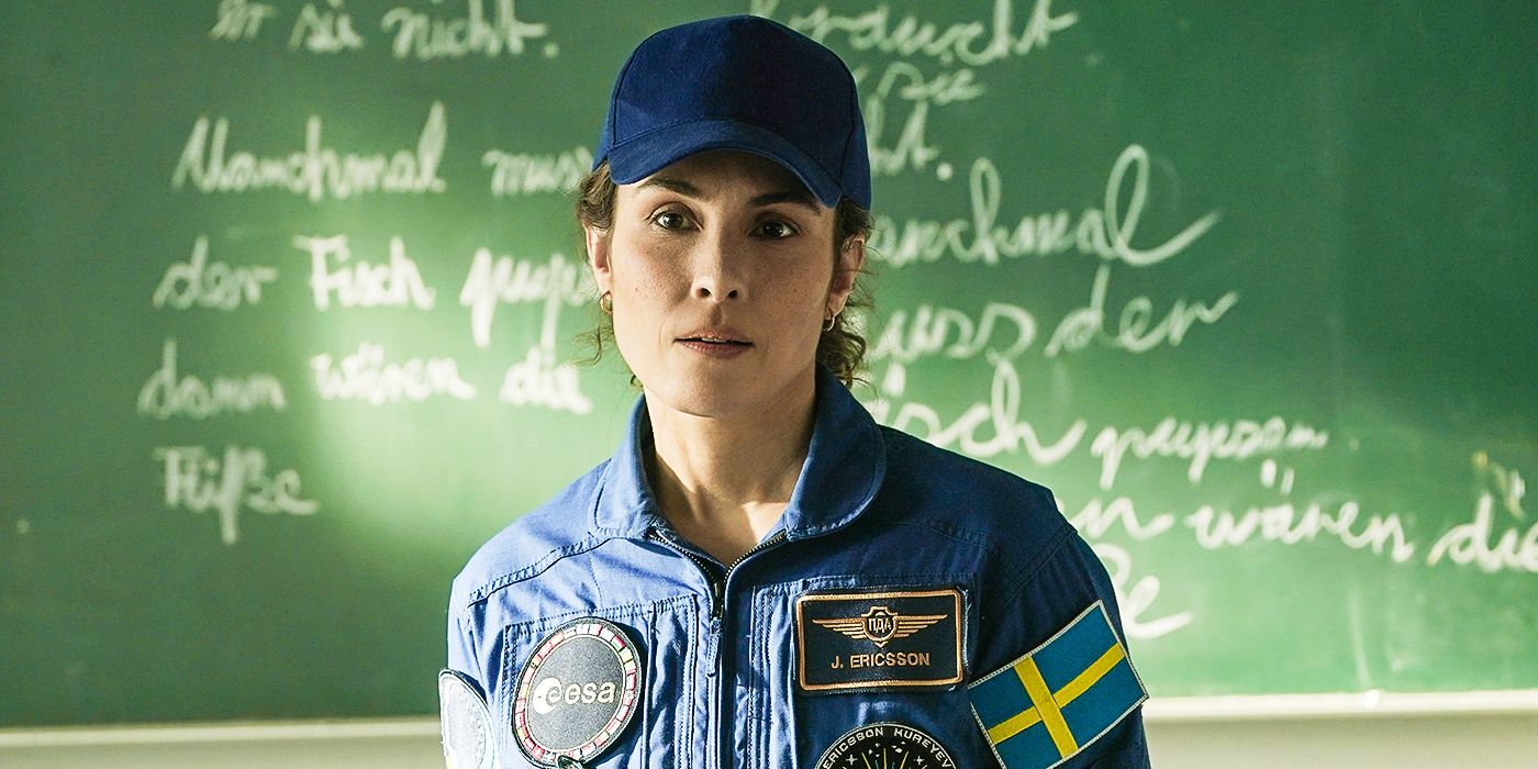 Noomi Rapace as Jo Ericsson wearing a hat standing in a classroom in front of a chalkboard in a still from Constellation Episode 4. 