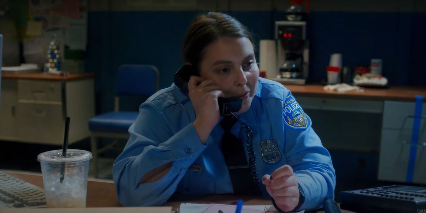 Beanie Feldstein as Sukie, on the phone, in her police uniform in Drive-Away Dolls