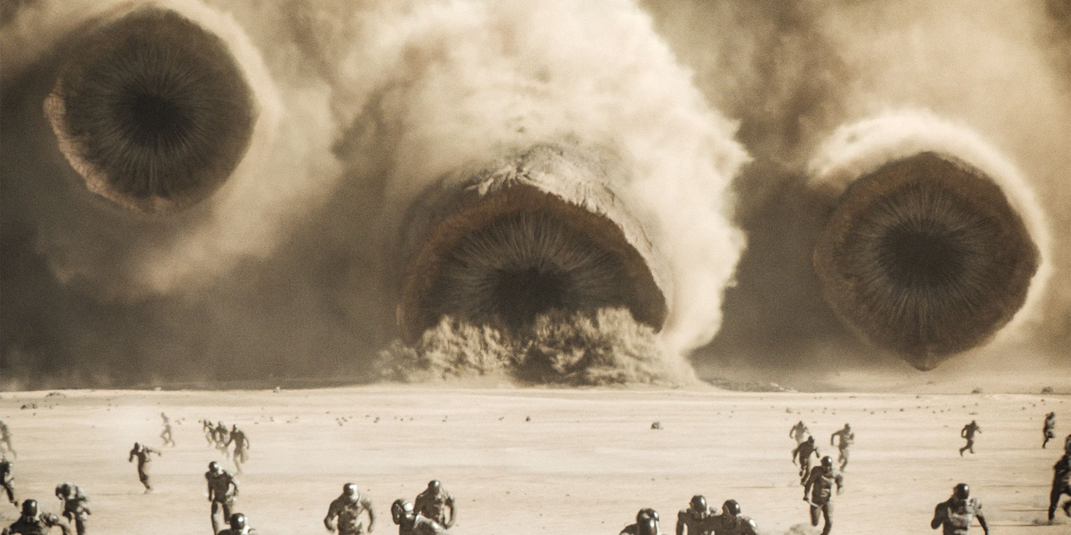 An image of people running away from three giant sandworms in the desert for Dune: Part Two