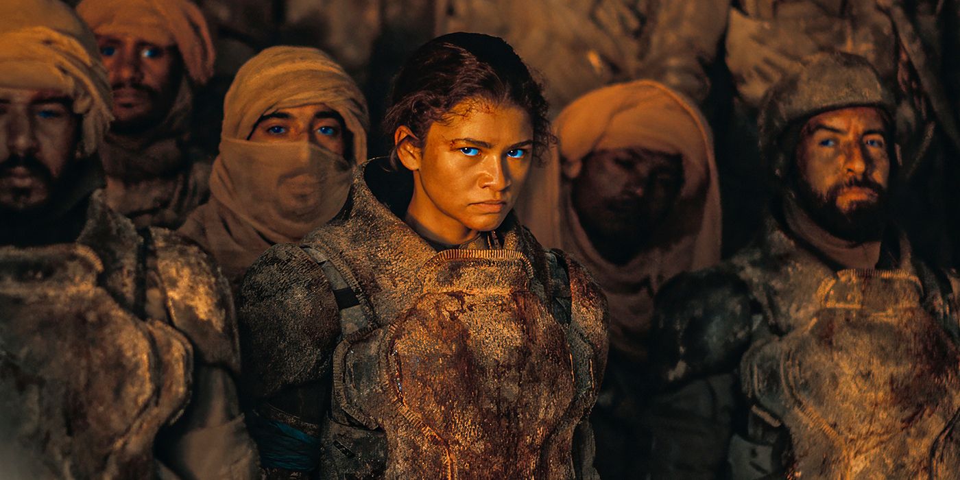 Zendaya as Chani staring with a determined express on her face in Dune: Part 2. chani's eyes are glowing blue from the spice. Behind Chani, there are other Fremen, wearing their stillsuits. 