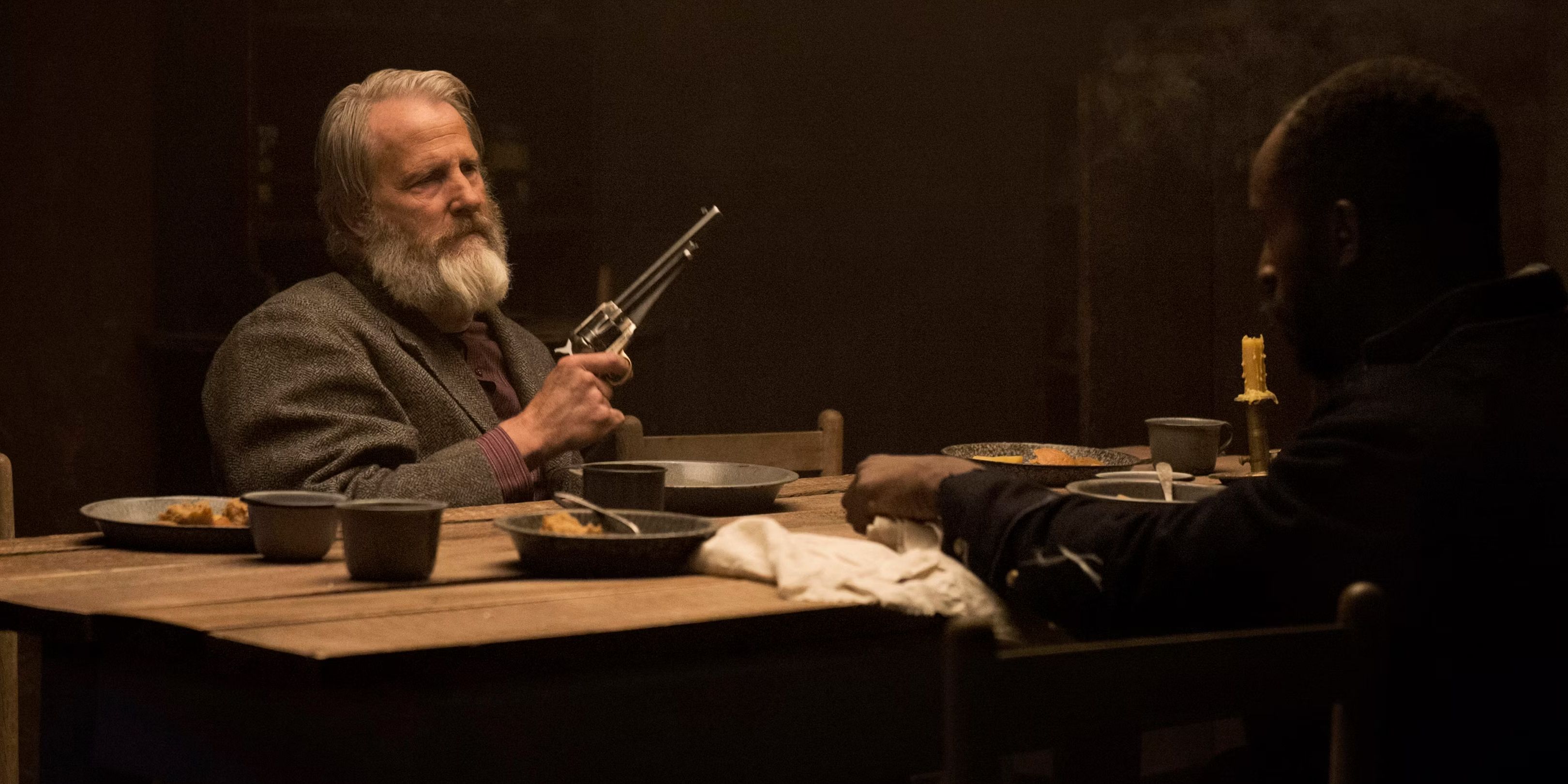 Frank Griffin (Jeff Daniels) sostiene un arma mientras está sentado en una mesa en Godless.