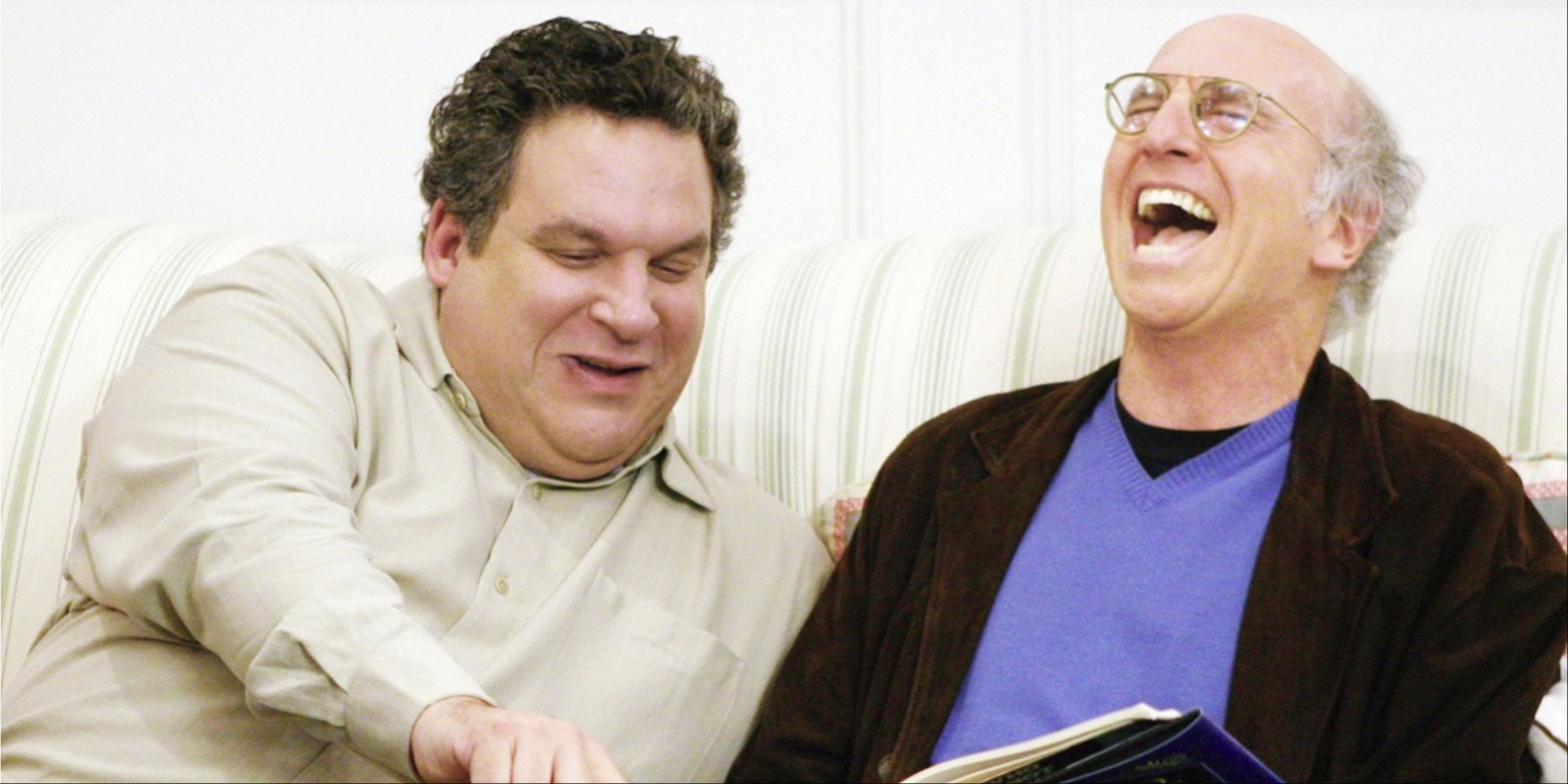 Larry David and Jeff Garlin laughing at a book on the couch in Curb Your Enthusiasm