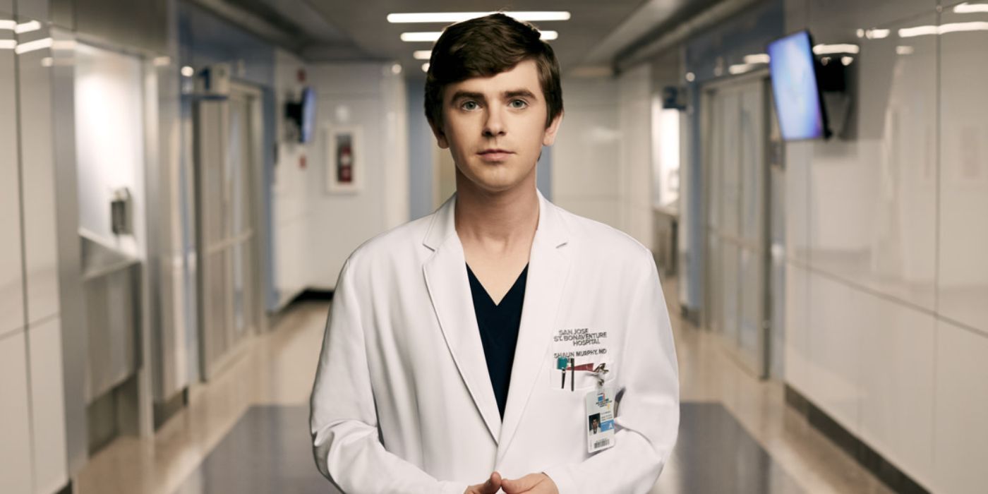 Freddie Highmore wearing a white lab coat and scrubs in the middle of a hallway in 'The Good Doctor'
