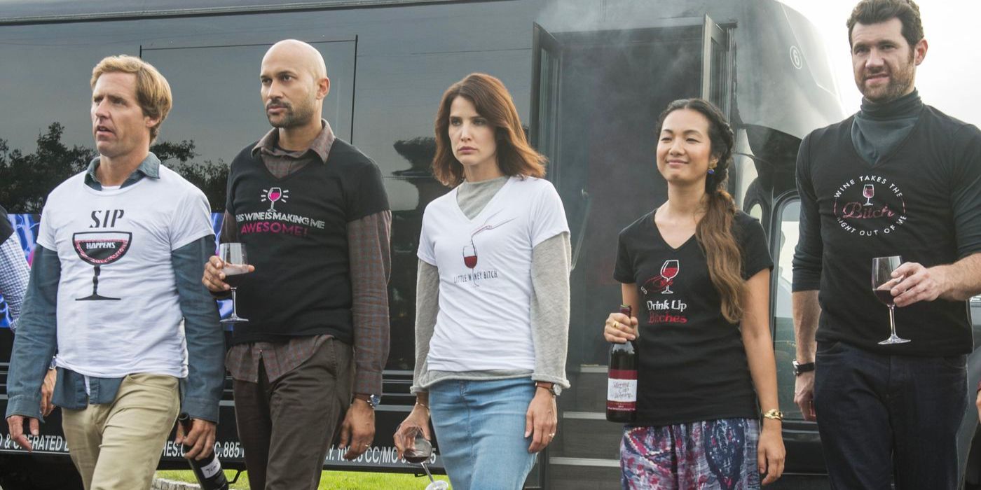 Five friends wear wine-themed t-shirts as they march together with glasses and bottles in hand.