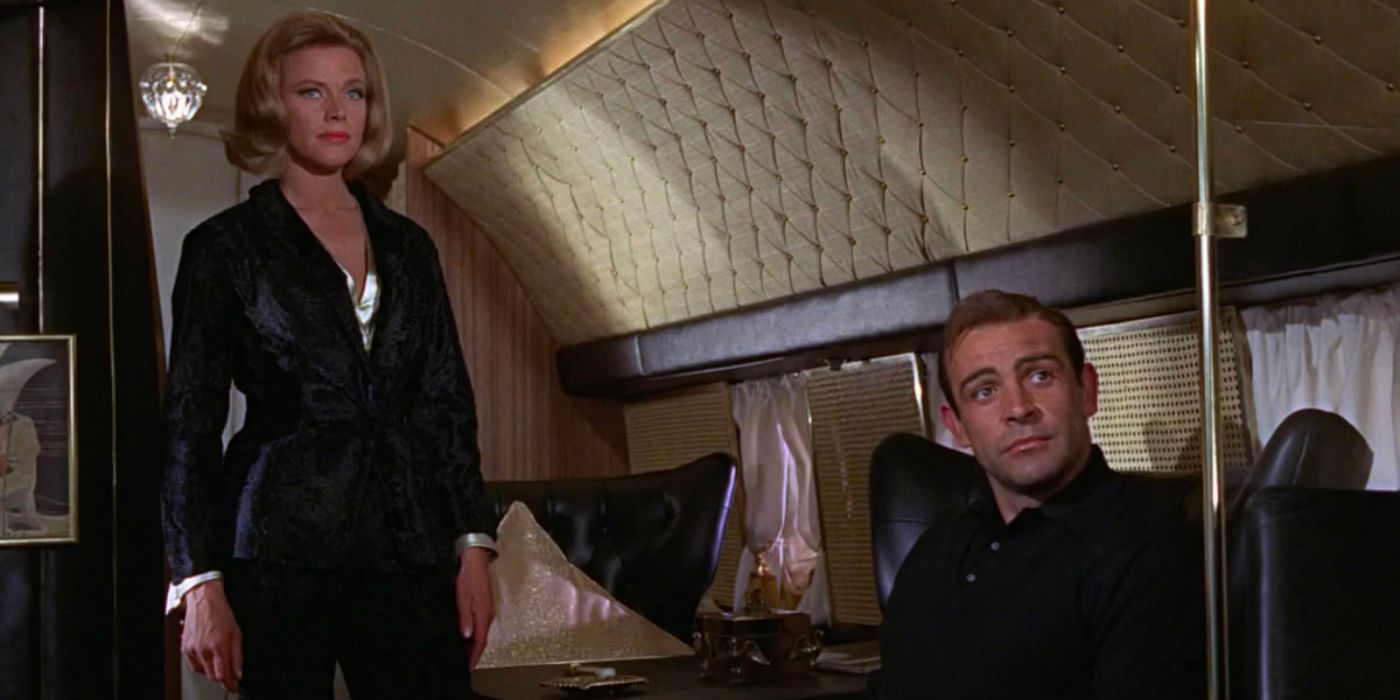 Pussy Galore (Honor Blackman) stands while James Bond (Sean Connery) sits, looking to ask for his signature drink.